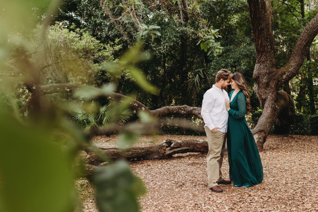 Engaged couple snuggles beneath moss covered tree